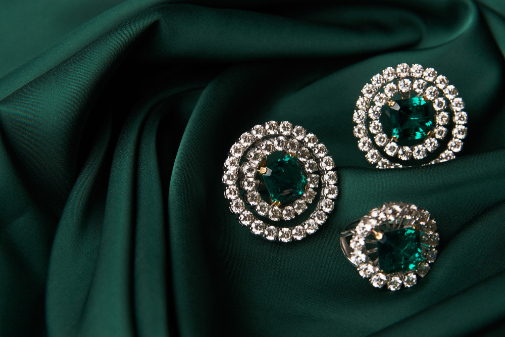 Emerald and diamond earrings and ring pair on green fabric background.