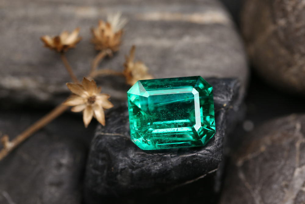Loose emerald cut emerald resting on stone.
